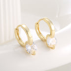 angled pair of round zirconia huggie earrings on a pale surface
