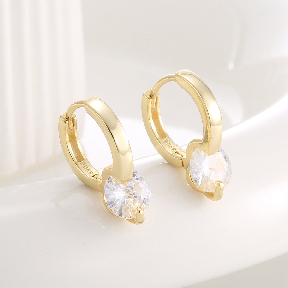 angled pair of round zirconia huggie earrings on a pale surface