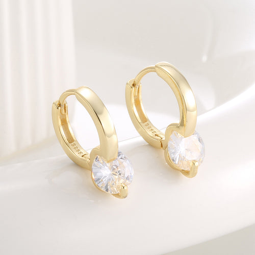 angled pair of round zirconia huggie earrings on a pale surface