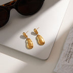 gold plated linked pebble drop earrings on a gray surface