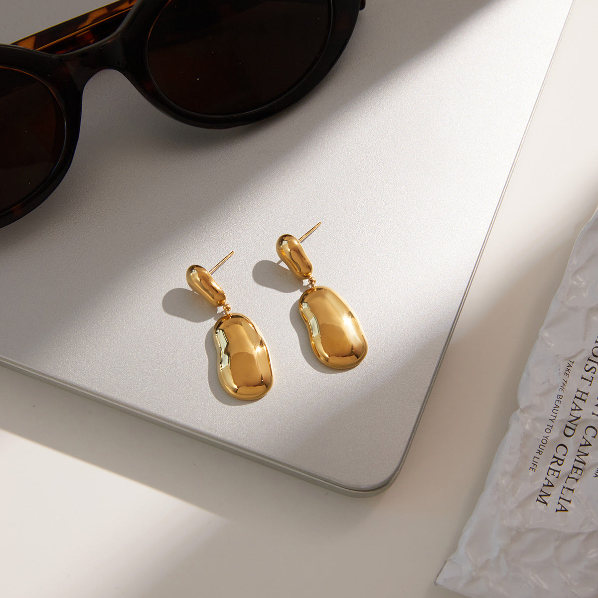 gold plated linked pebble drop earrings on a gray surface