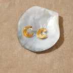 Pair of textured crescent moon earrings displayed on a shell prop