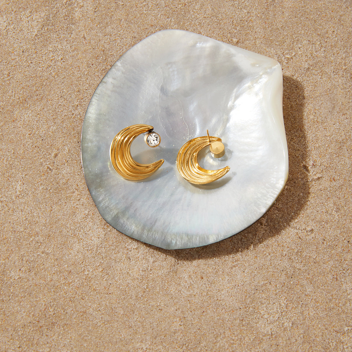 Pair of textured crescent moon earrings displayed on a shell prop
