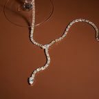 clear-stone Y necklace with pear-shaped tip arranged by a glass