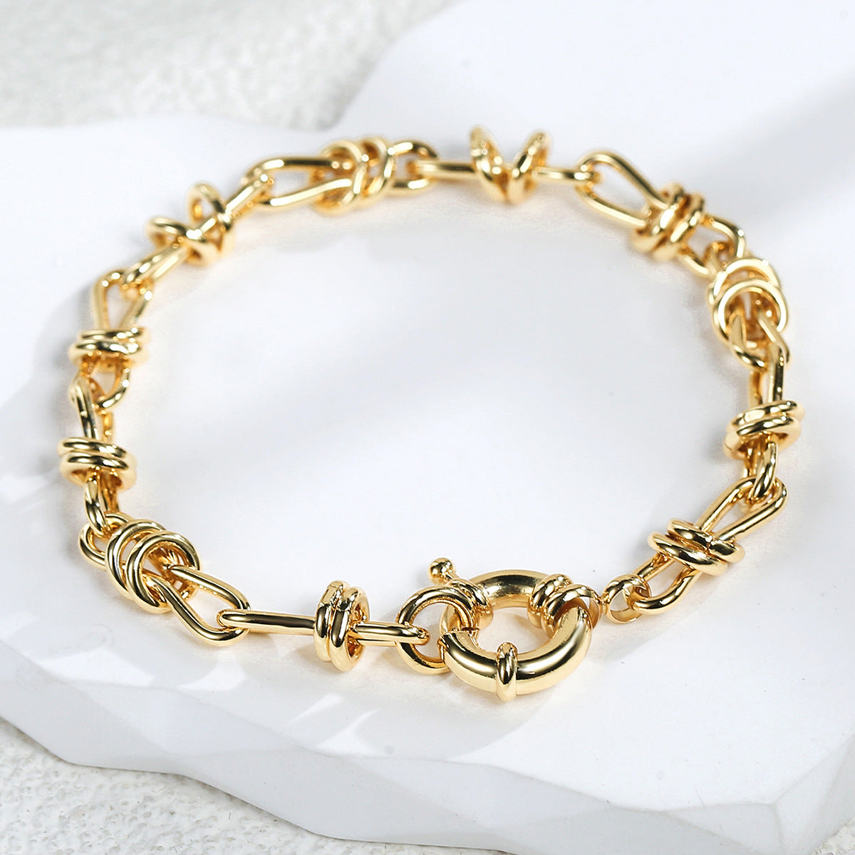 gold plated bow-knot chain bracelet arranged on a pale stone surface