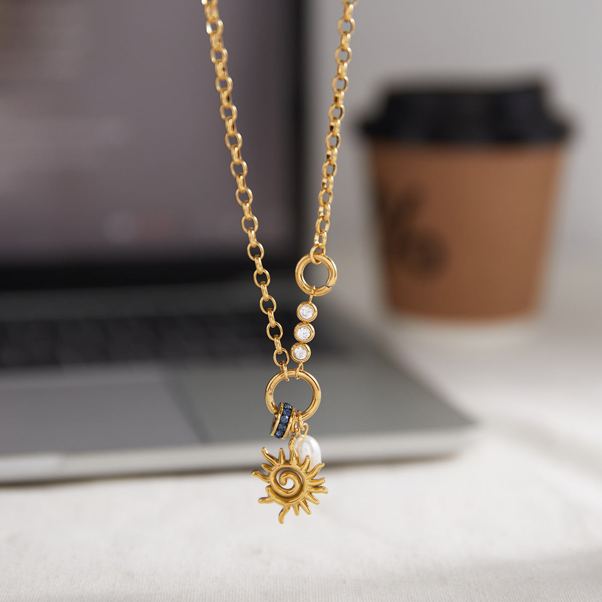 spiral sun pearl charm necklace beside a laptop