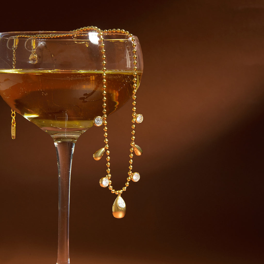 gold plated teardrop station necklace draped over a glass