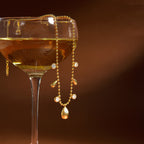 gold plated teardrop station necklace draped over a glass