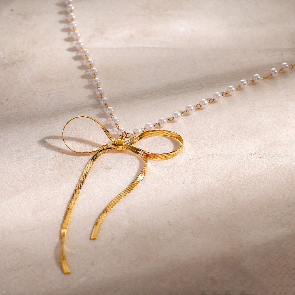 Open ribbon bow necklace with small white beads on pale stone