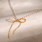 Open ribbon bow necklace with small white beads on pale stone