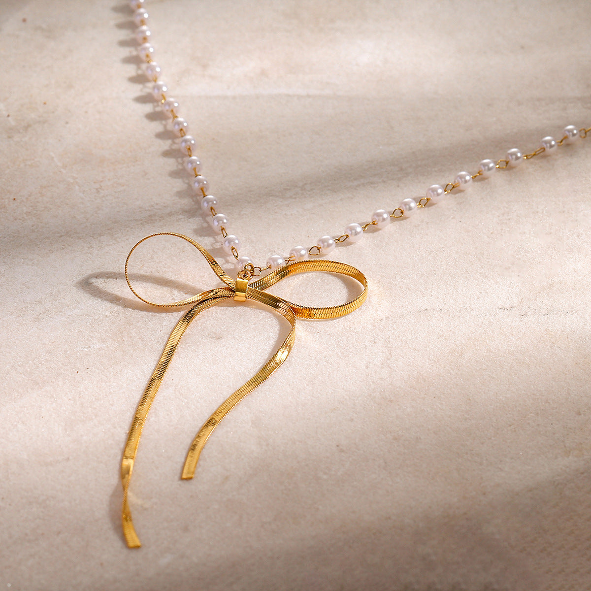 Open ribbon bow necklace with small white beads on pale stone