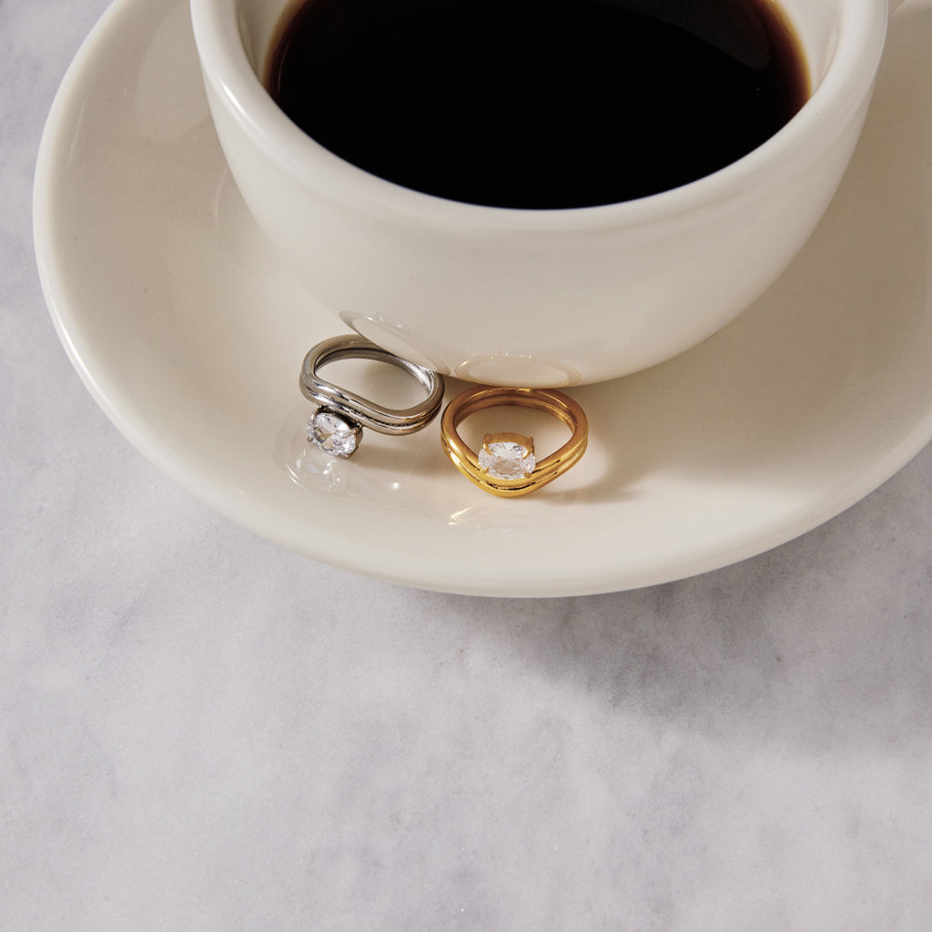 Two wavy solitaire rings displayed beside a cup