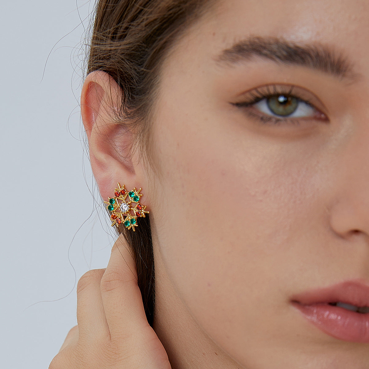 Red and green snowflake stud earrings shown on the ear