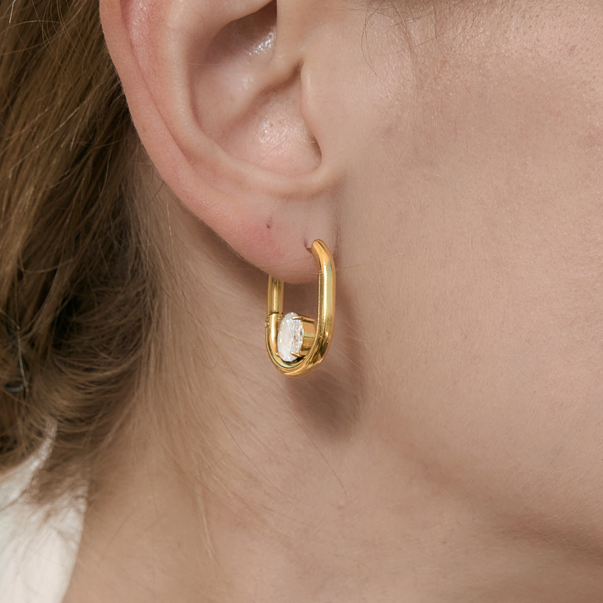 Gold finish U-shaped clear-stone earring worn close-up