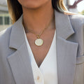 gold plated stainless steel sunburst disc pendant necklace worn with a blazer
