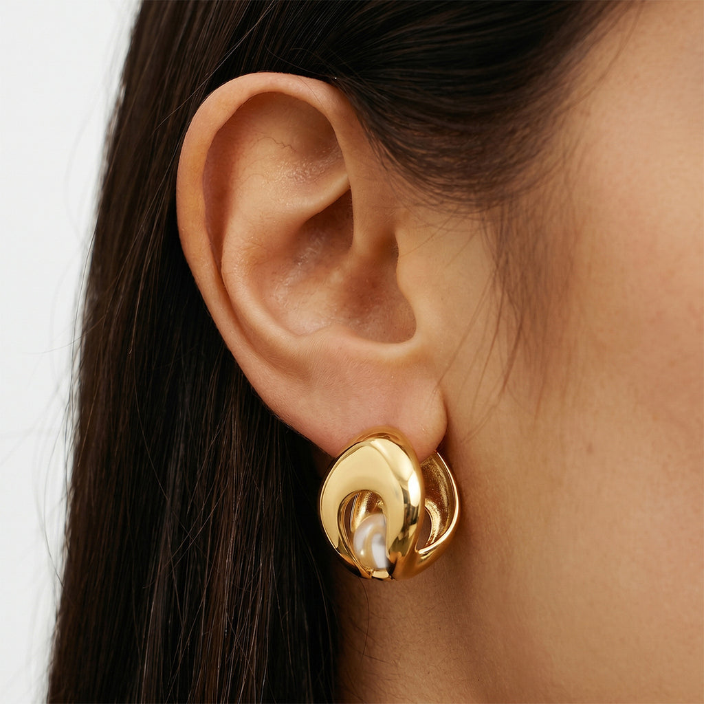 Sculpted gold tone earring with white bead worn close-up