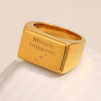 gold plated rectangular message signet ring on a pale backdrop