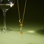 Gold-finish celestial Y necklace hanging against a green background
