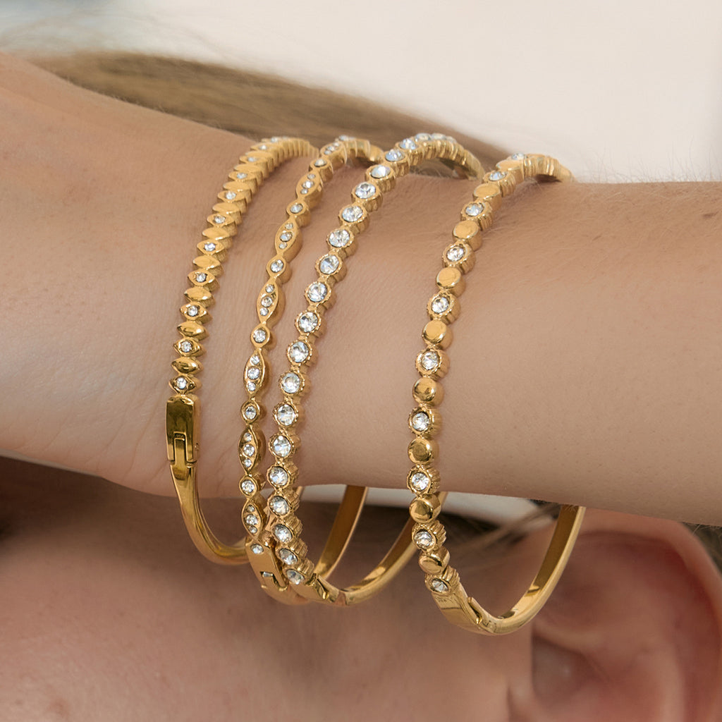 Four clear accent gold-tone stainless steel bangles stacked on a wrist