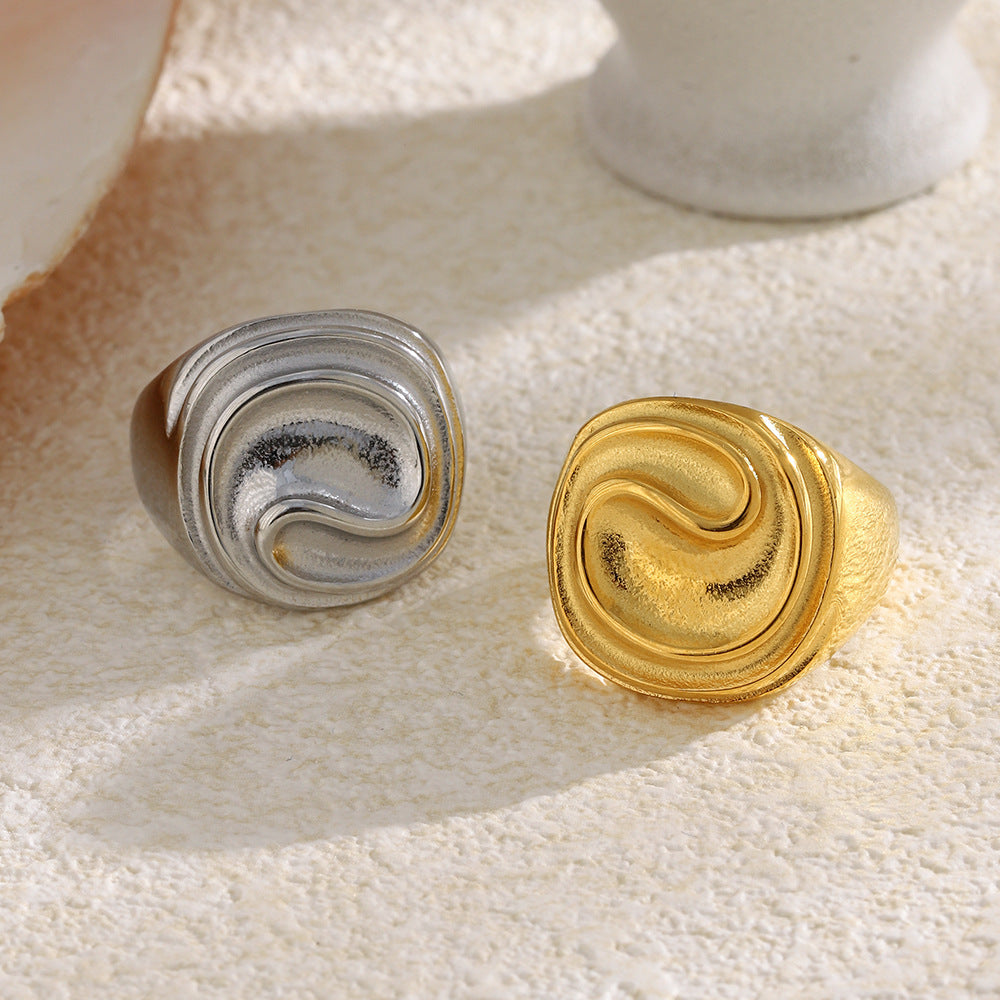 two stainless steel sculptural signet rings on a stone surface