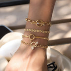 Four gold-tone chain bracelets stacked on a wrist