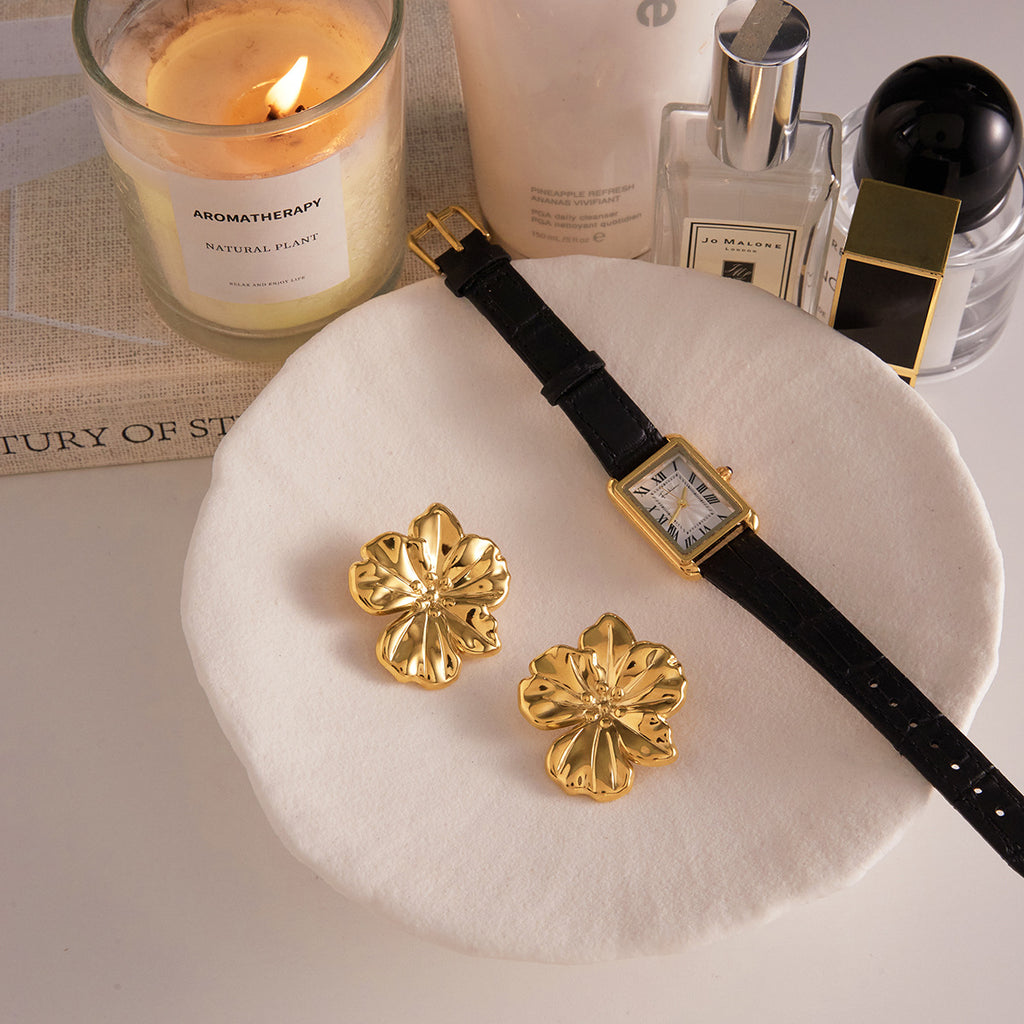 Gold plated flower earrings styled beside a watch on a tray