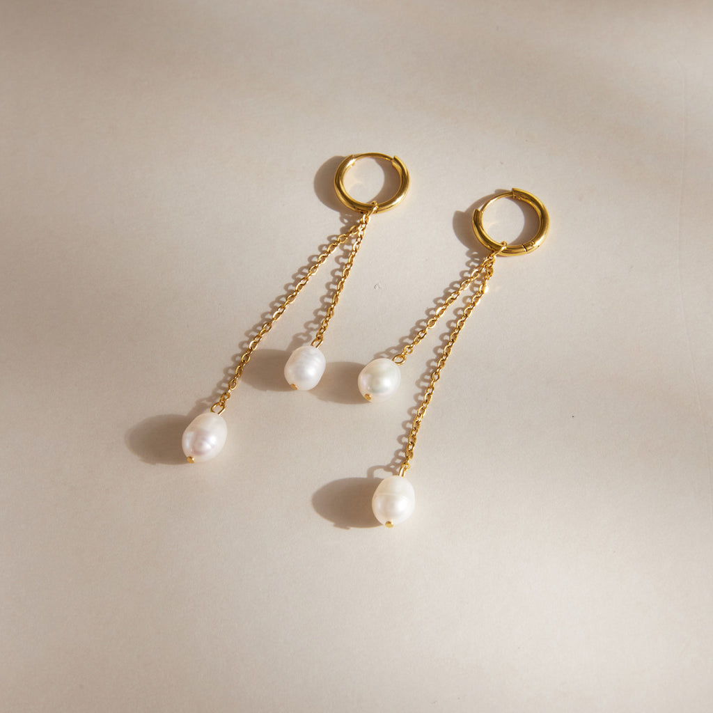 White pearl-look chain earrings arranged on a pale tray