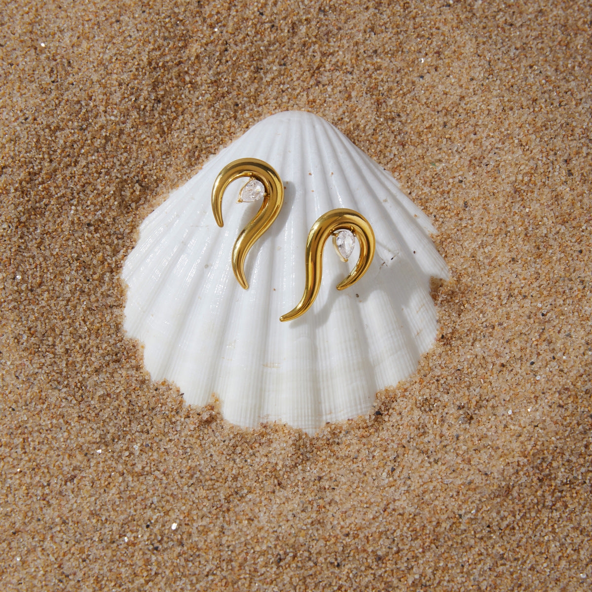 Pair of flame-curve earrings displayed on a shell