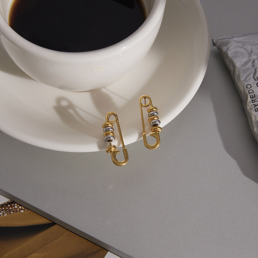 pair of two-tone safety-pin stud earrings beside a coffee cup