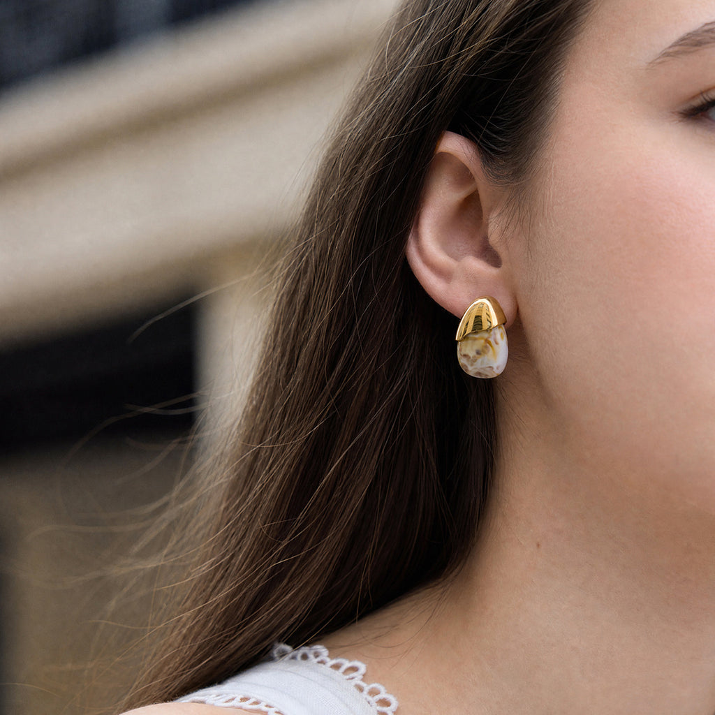 White marbled resin stud with gold tone cap worn on an ear
