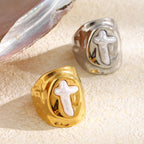 two finish cross signet rings styled beside a shell