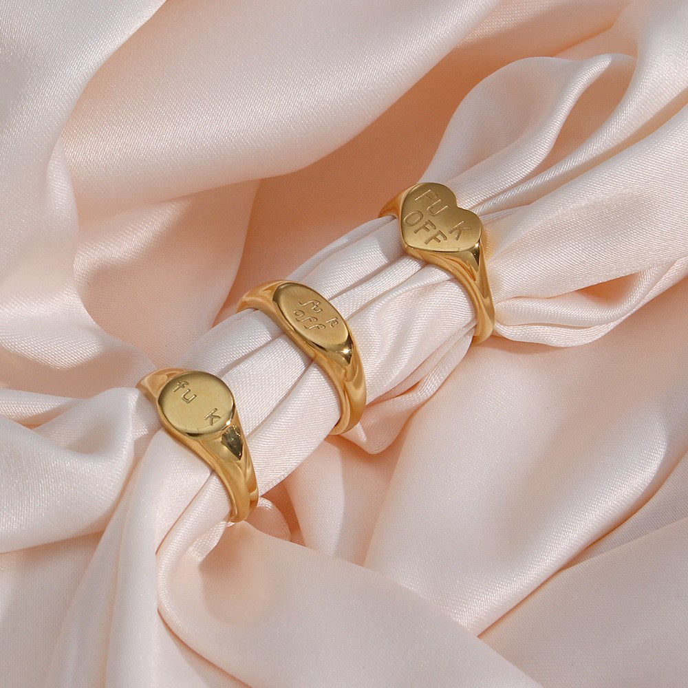 Three gold tone slogan signet rings displayed on fabric