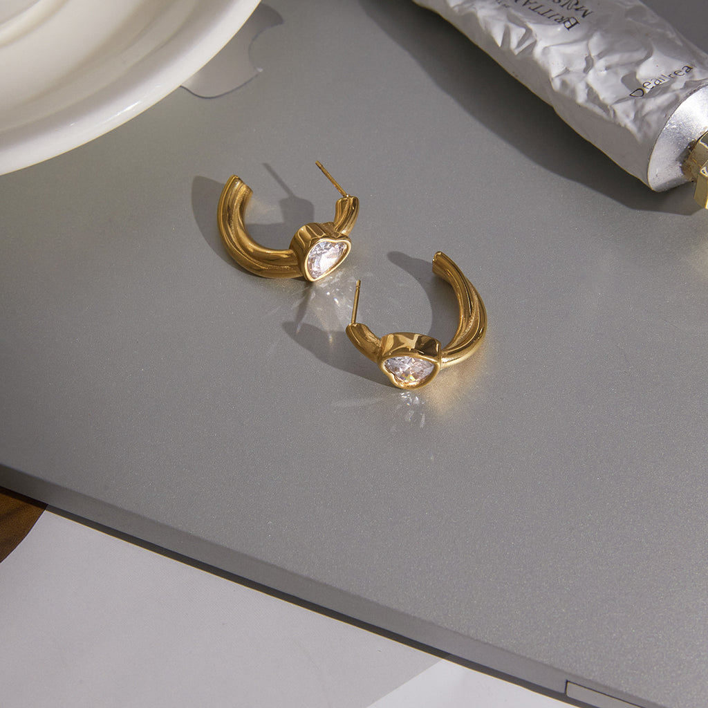 Gold-tone heart hoop earrings arranged on a reflective surface