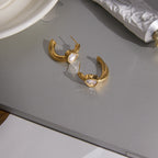 Gold-tone heart hoop earrings arranged on a reflective surface