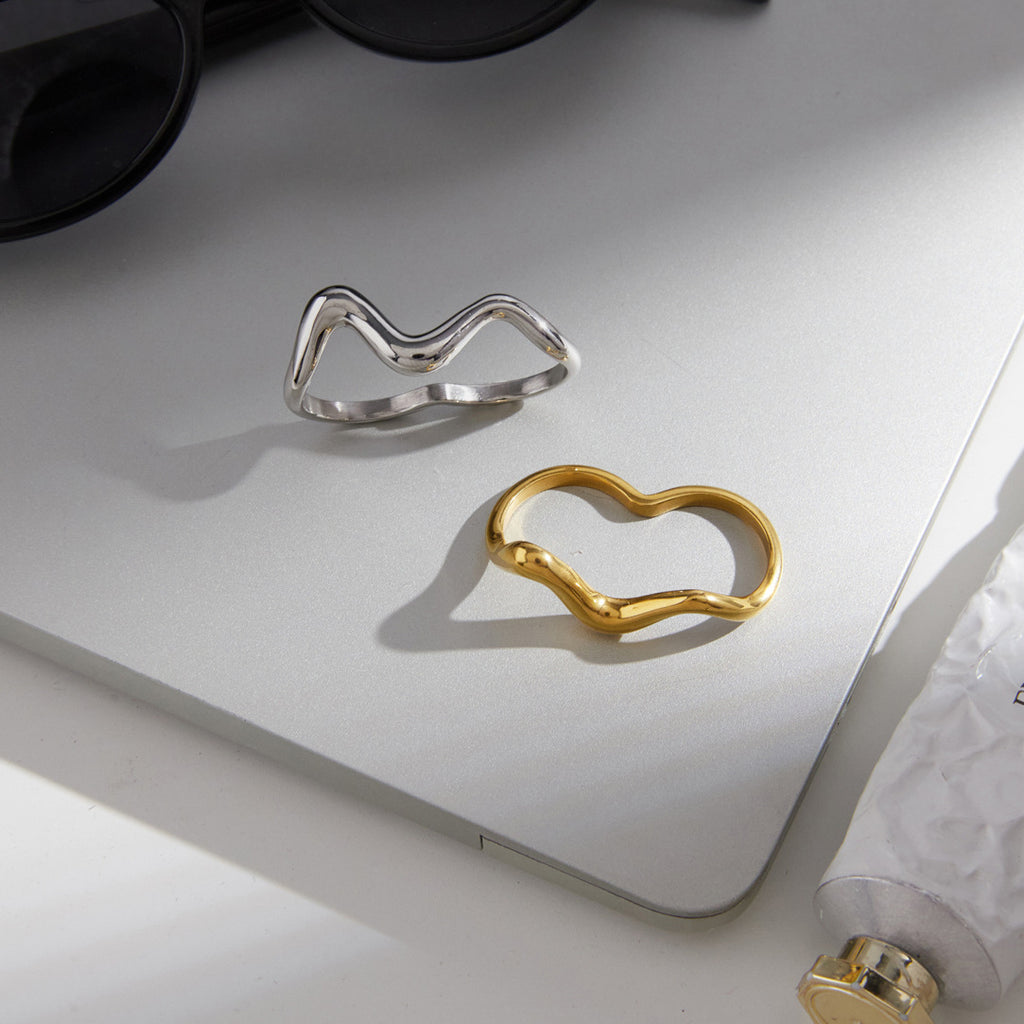 Two metallic versions of the wavy ring on a gray surface