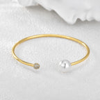 pearl-style and clear stone open bangle on white textured fabric
