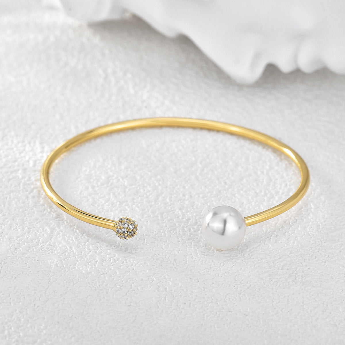 pearl-style and clear stone open bangle on white textured fabric