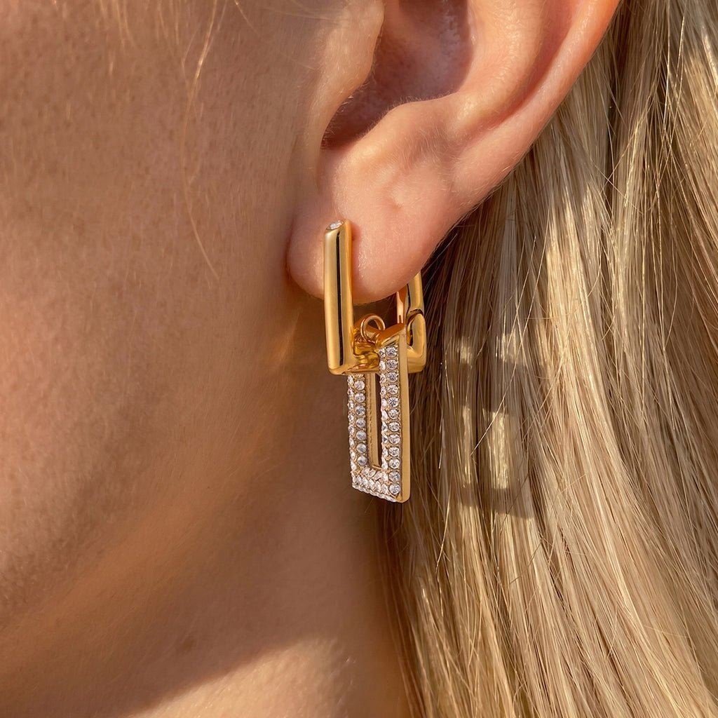 Gold tone open rectangle earring worn on an ear
