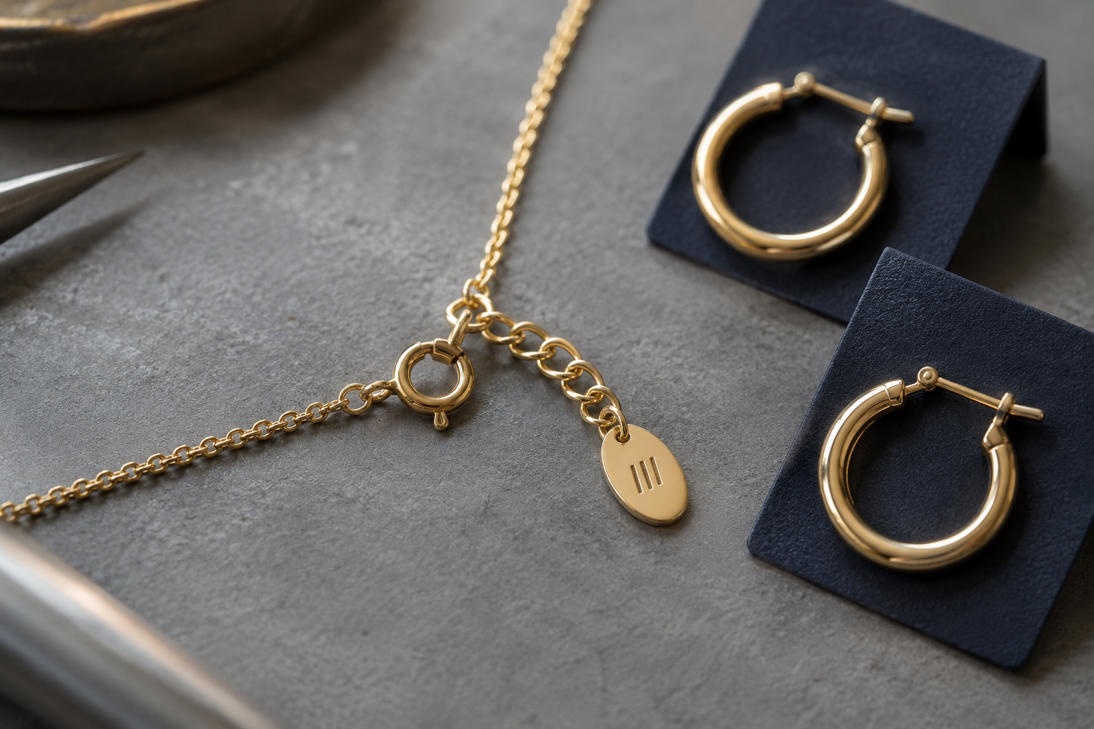 Illustrative necklace clasp and engraved branding tag beside navy jewelry cards