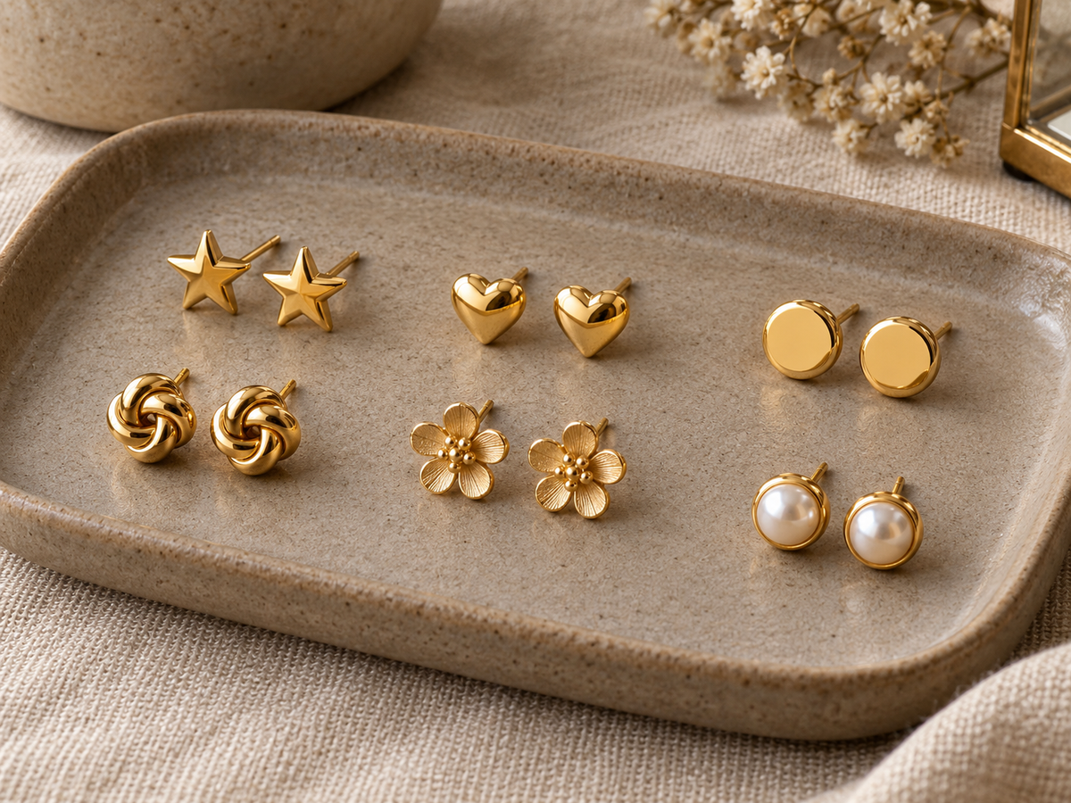 Gold plated star, heart, disc, flower and pearl stud earrings arranged on a taupe tray