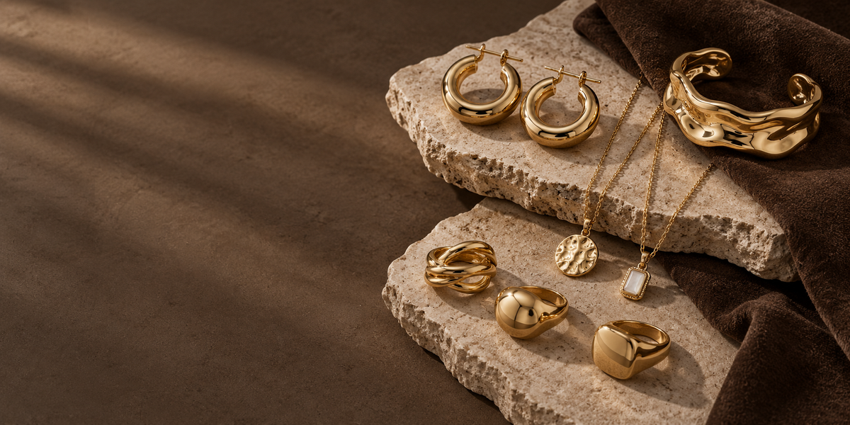 Gold-tone earrings rings necklaces and cuff arranged on warm stone