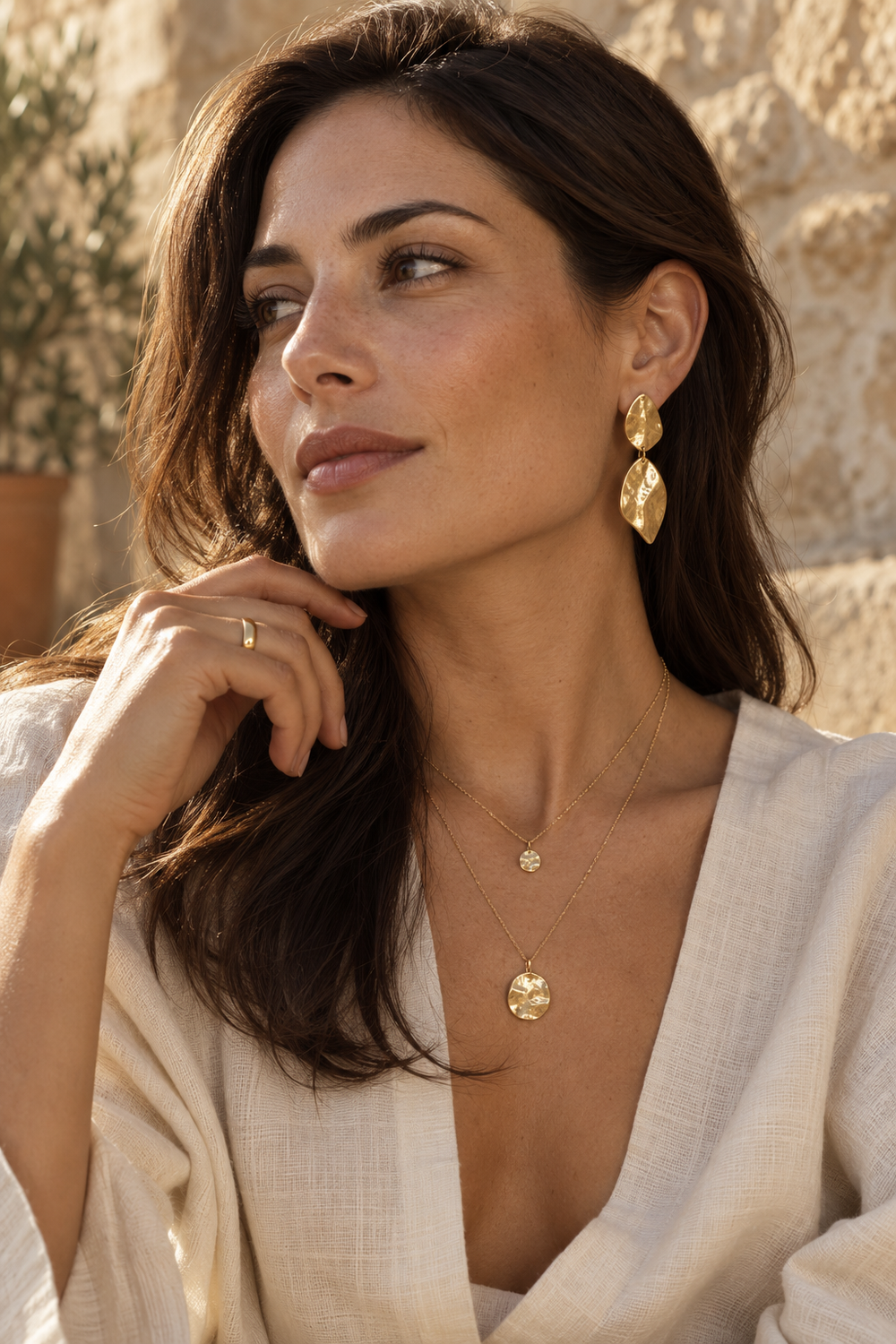 Model wearing sculptural gold-tone earrings and layered pendant necklaces