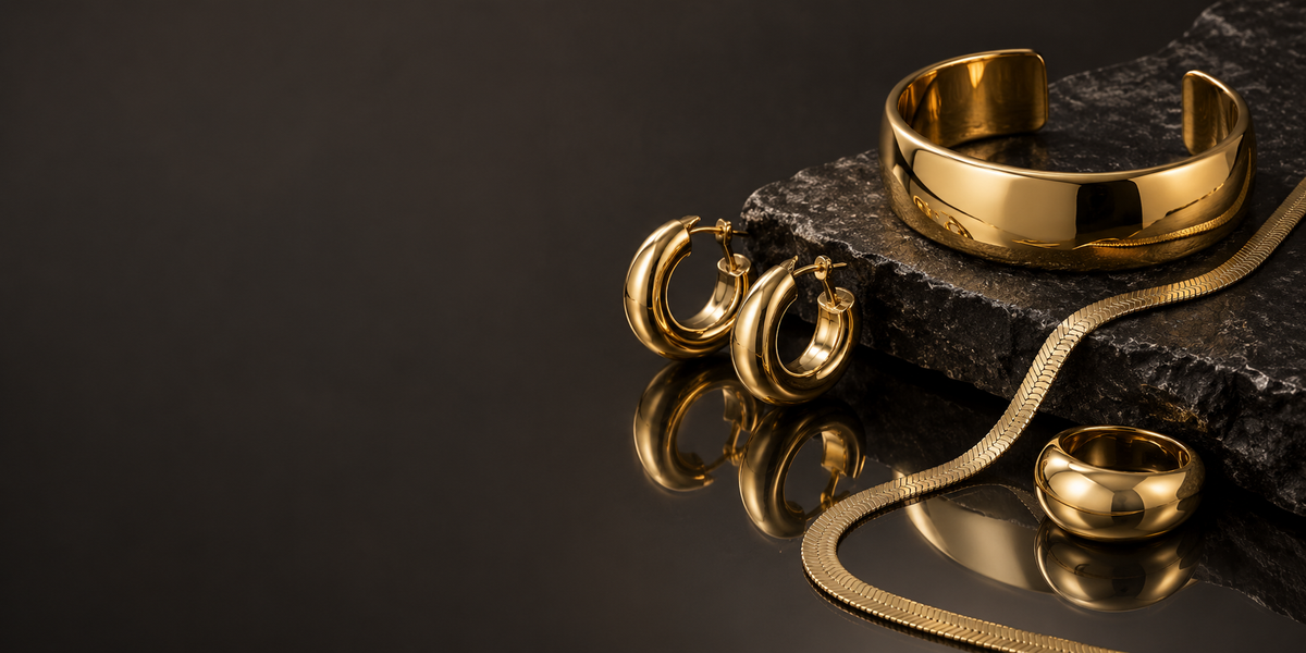 Polished gold-tone jewelry on dark stone and smoked mirror